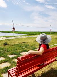 Man sitting on bench on field against sky