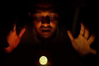 Close-up of man looking at illuminated ball in darkroom