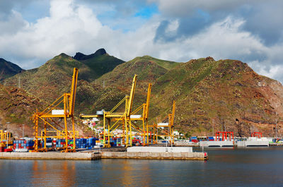 Commercial dock by mountain against cloudy sky