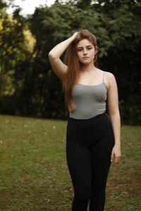 Portrait of beautiful woman with hand in hair standing on grassy field at park