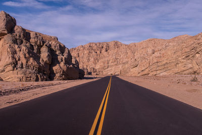 Empty road along rocky mountains against sky