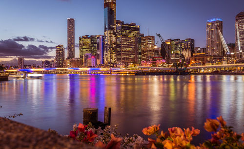 Illuminated city by river against sky at night