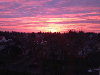 Silhouette trees and houses against sky at sunset