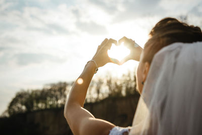 Rear view of woman holding heart shape against sky