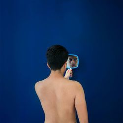 Shirtless young man standing against blue background