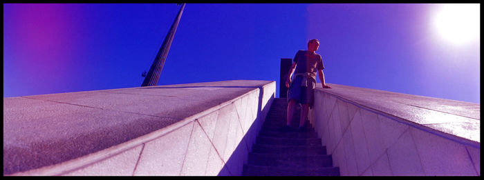 Low angle view of man standing on steps against clear blue sky