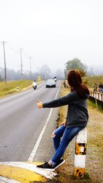 Side view of young woman on road against sky