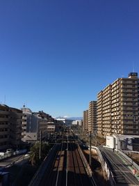 Railroad tracks in city against clear blue sky