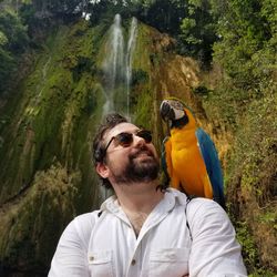 Portrait of young man in the rain forest with a macaw parrot