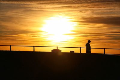 Rear view of silhouette woman walking on beach against sky during sunset