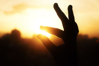 Close-up of silhouette hand against sunset sky
