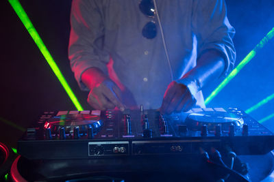 Midsection of man operating sound mixer at nightclub