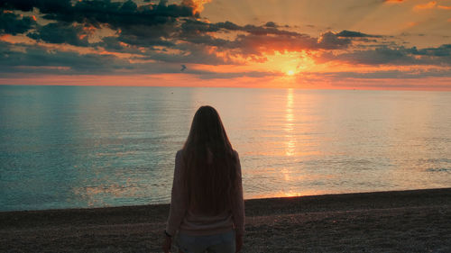 Rear view of woman looking at sea during sunset
