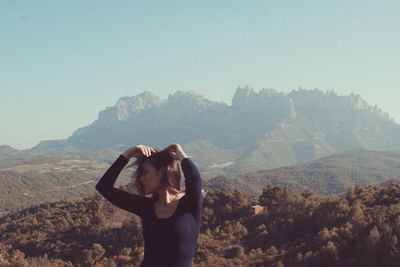 Woman with hands in hair standing against mountains and sky during sunny day
