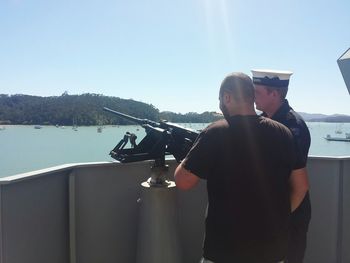 Rear view of men on shore against clear sky