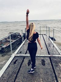 Full length rear view of woman standing on railing against sea