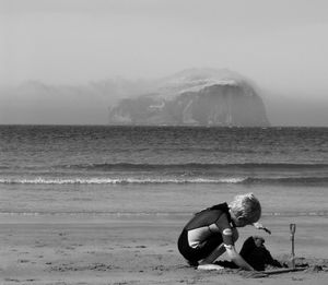 Boy making sandcastle at beach against bass rock in sea