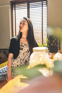 Young woman looking away while sitting on table at home