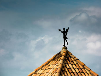 Low angle view of statue on roof against sky