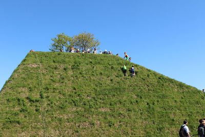 Low angle view of people on green pyramid against clear blue sky