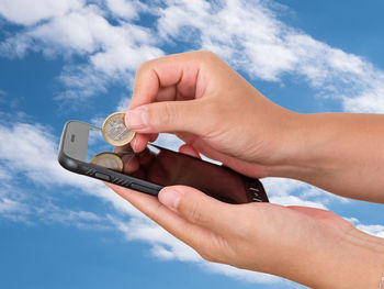 Midsection of person holding mobile phone against sky