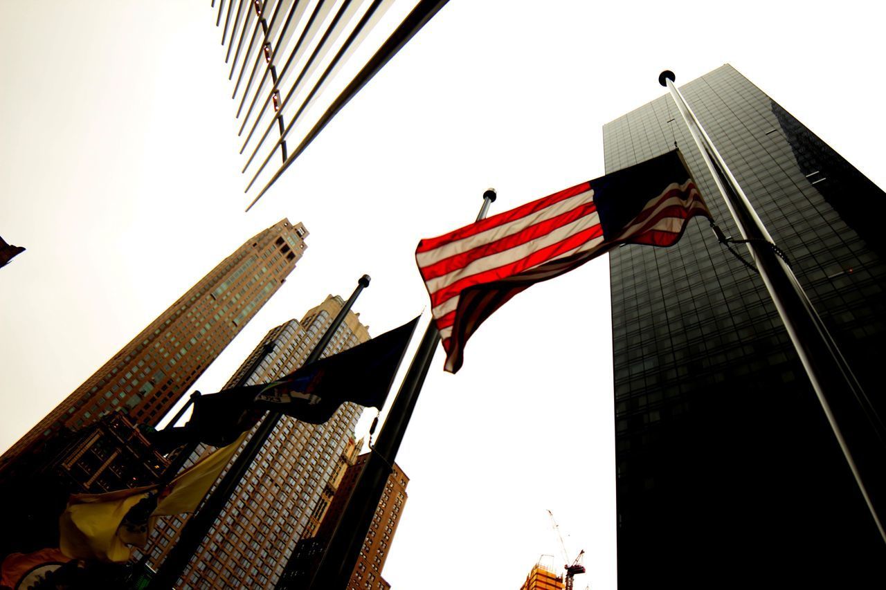 LOW ANGLE VIEW OF FLAG AGAINST BUILDINGS IN CITY AGAINST SKY