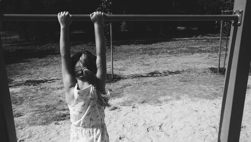 Rear view of girl hanging on monkey bars at playground