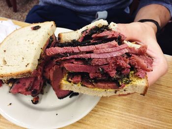 Cropped image of hand holding pastrami sandwich over table