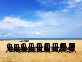 Wooden chairs on beach against sky