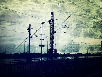 Low angle view of electricity pylon against cloudy sky