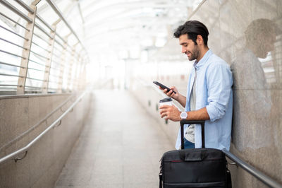 The man uses the smartphone while the other hand holds a cup of coffee.