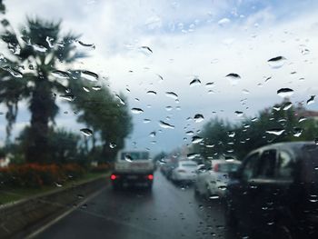 Cars on road against sky seen through wet car windshield