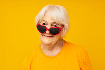 Portrait of senior woman wearing novelty glasses against yellow background