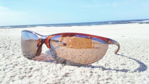 Close-up of sunglasses on beach against sky on sunny day