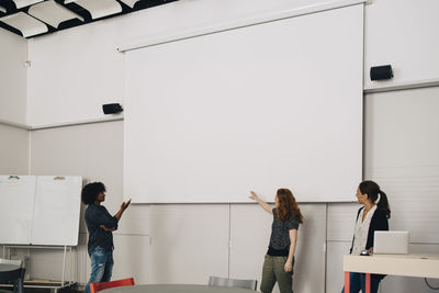 Confident multi-ethnic technicians giving presentation over blank projection screen at creative office