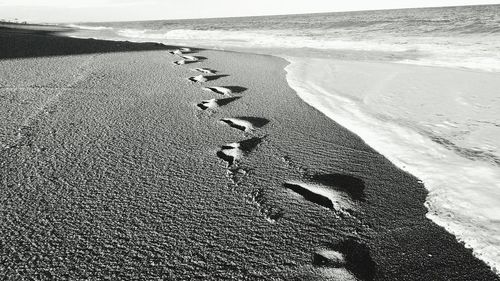 Footprints on sand at beach against sky