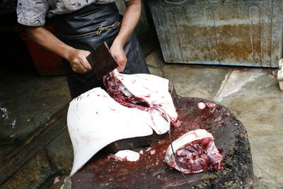 Midsection of butcher cutting stingray on wood at market