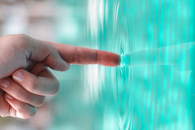 Cropped hand touching rippled water in swimming pool