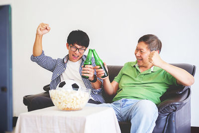 Cheerful father and son cheering while watching tv set at home