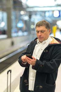 Man using mobile phone while standing at railroad station platform