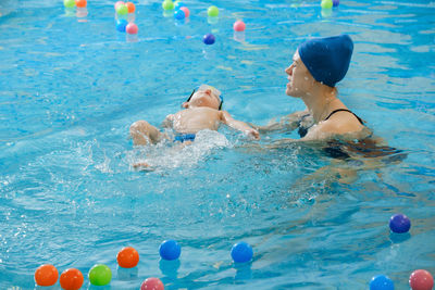 Toddler child learning to swim in indoor swimming pool with teacher. floating in the water