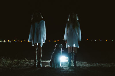 Full length of female friends standing by dog on land at night