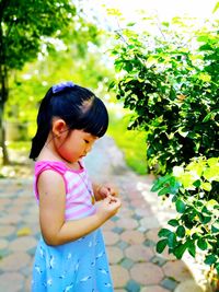 Side view of girl standing by plant in park