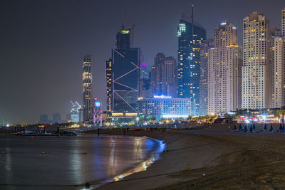 Illuminated modern buildings in city against sky at night