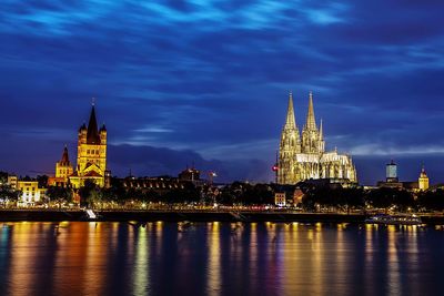 Illuminated buildings by river against sky in city