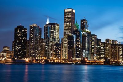 Illuminated buildings by city against sky at dusk