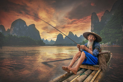 Portrait of man sitting by mountain against sky during sunset