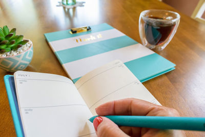 Cropped hand of woman writing in book on table