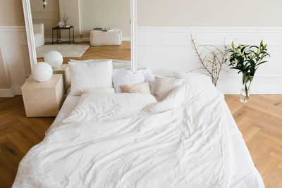 A double bed with white linens and beige pillows in a bright scandinavian bedroom