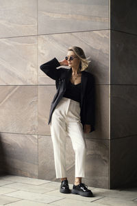 Young woman wearing sunglasses standing against wall